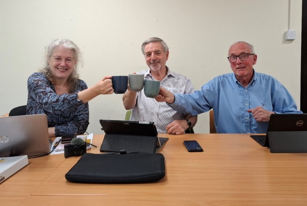 Three people around laptops with mugs of tea.